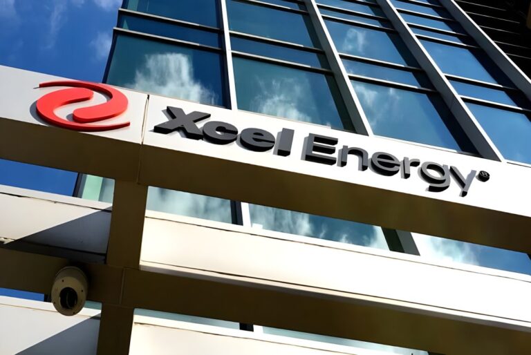 Xcel Energy logo and signage on the exterior of a glass office building reflecting a blue sky with clouds.