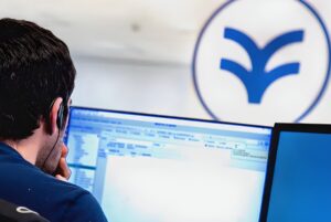 A technician wearing a headset monitors data on a computer screen in front of a blue Idrica logo.