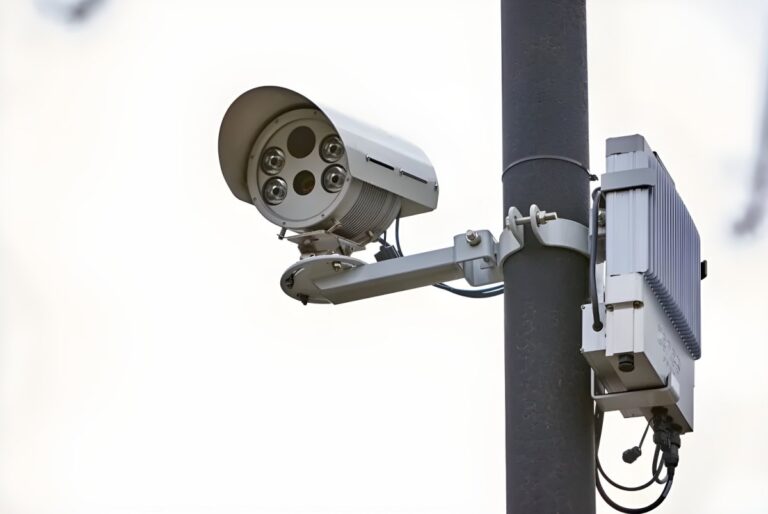 Yunex Traffic advanced traffic camera and sensor unit mounted on a dark grey utility pole against a white sky.