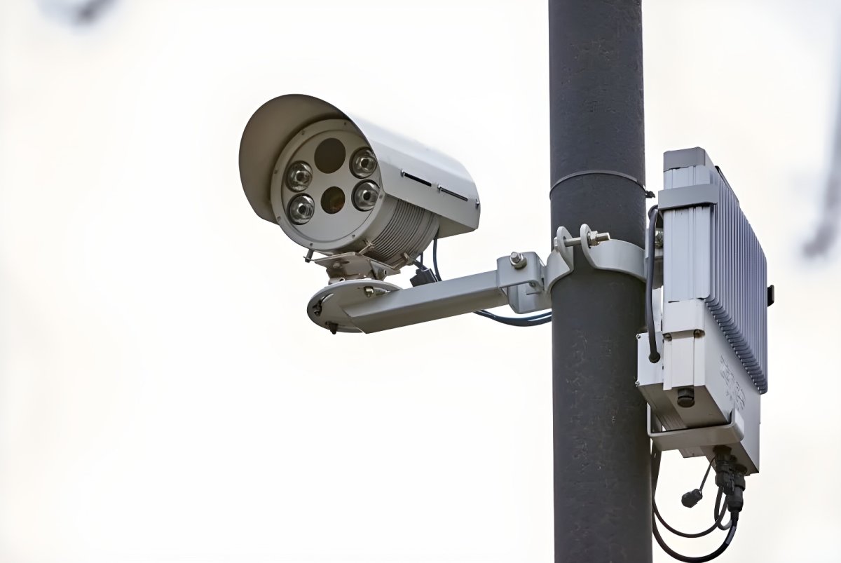 Yunex Traffic advanced traffic camera and sensor unit mounted on a dark grey utility pole against a white sky.