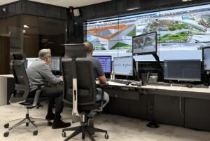 Two operators in a control room monitor water infrastructure data and maps on a large video wall and desktop screens.