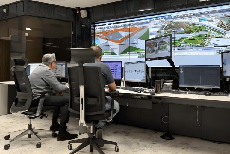 Two operators in a control room monitor water infrastructure data and maps on a large video wall and desktop screens.