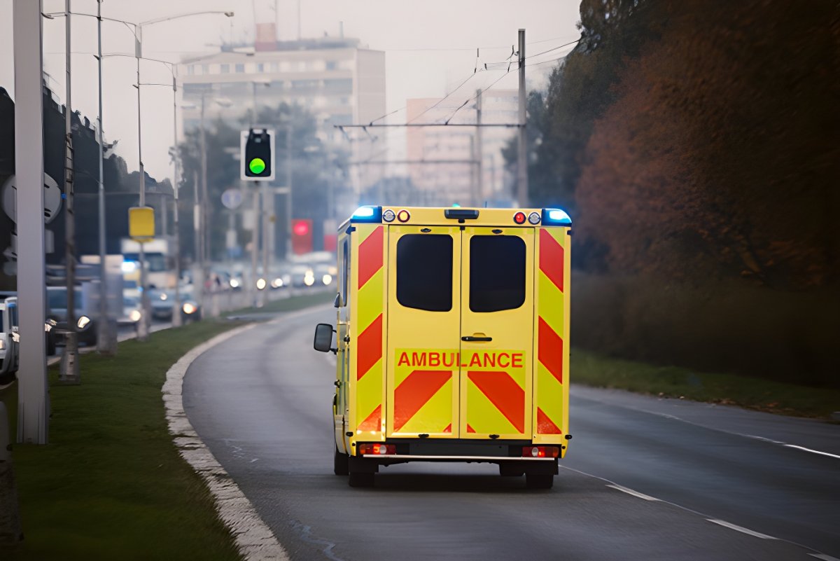 Rear view of a yellow ambulance with flashing blue lights driving toward a green traffic signal on a city road.