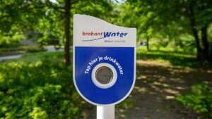 Brabant Water public drinking water tap station in a park with green trees in the background.