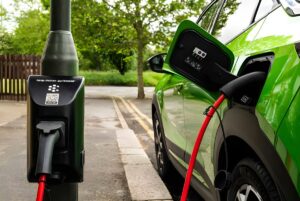 A green electric car charging at a char.gy lamp post bollard on a residential street.