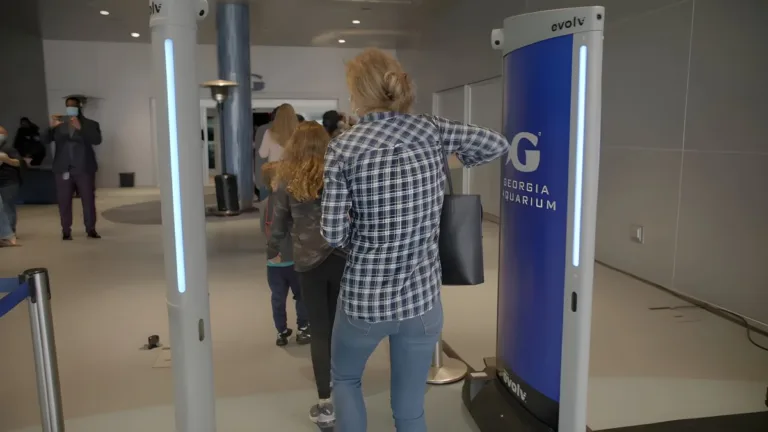 People walking through Evolv Technology Express security screening towers at the Georgia Aquarium entrance.