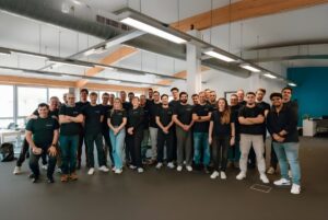 A large group of LIFEPOWR employees wearing black branded t-shirts standing in a modern open-plan office.