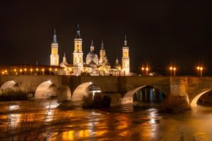 Night view of the Basilica del Pilar and the illuminated Puente de Piedra bridge over the Ebro River in Zaragoza, Spain.