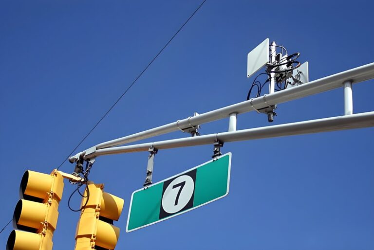 Wireless IoT sensors and communication antennas mounted on a metal traffic signal gantry against a clear blue sky.
