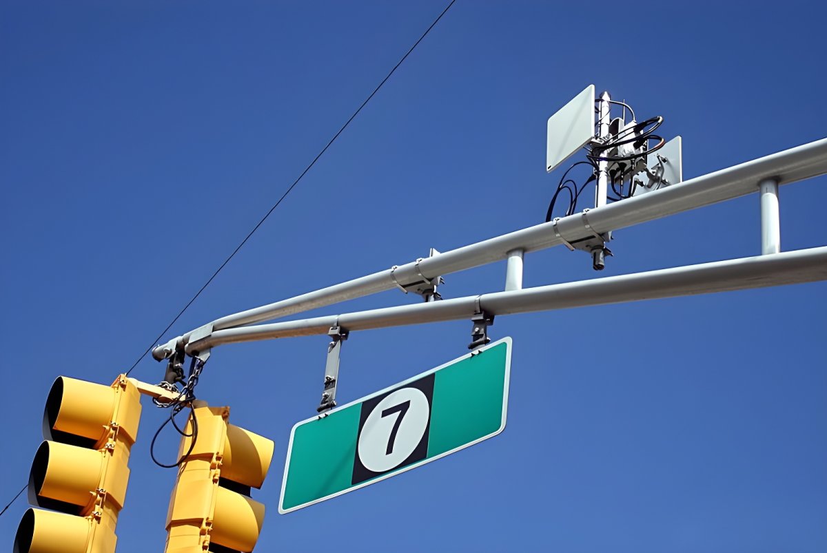 Wireless IoT sensors and communication antennas mounted on a metal traffic signal gantry against a clear blue sky.