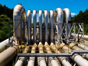 Large industrial steel pipes and vertical U-shaped conduits at a water treatment facility with metal catwalks.