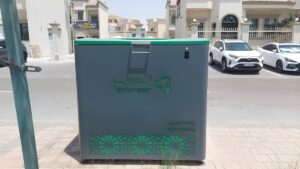 A grey and green Tadweer Group smart waste bin on a residential sidewalk in Abu Dhabi.