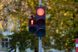 Red traffic light and red pedestrian signal on a metal pole with blurred autumn trees in the background.
