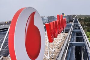 Red Vodafone signage and logo mounted on a rooftop next to solar panels and industrial infrastructure.