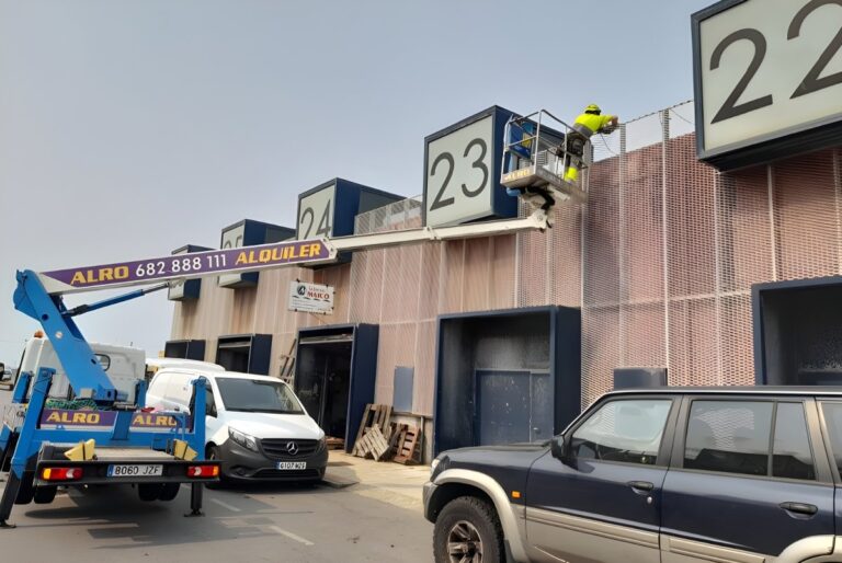 Worker in a high-visibility vest on a cherry picker installing lighting on a Portos de Galicia building in Rianxo.